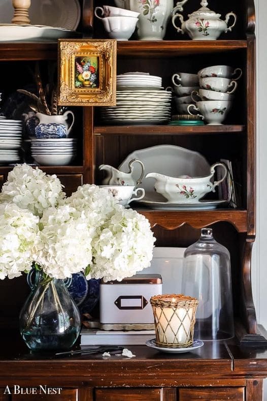 Vintage china and fresh flowers styled on a kitchen cabinet for a timeless, collected interior
